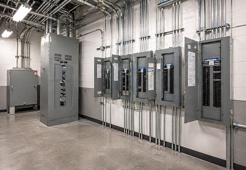 Clean commercial electrical room with multiple breaker panels and organized conduit systems along a wall in an industrial facility