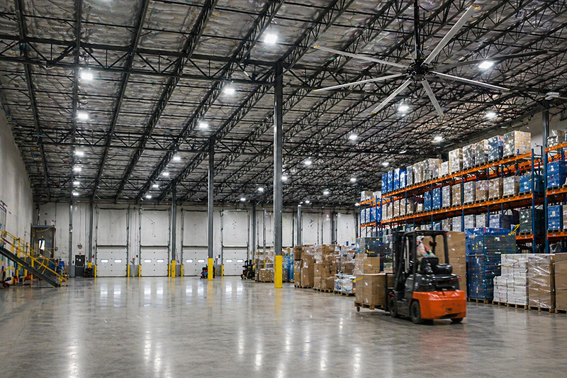 Large commercial warehouse interior with HVLS ceiling fan, LED lighting, and pallet storage showcasing energy-efficient upgrades in Southern California