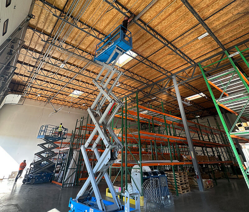Technicians performing electrical and lighting installation in a commercial warehouse facility using scissor lifts in Southern California